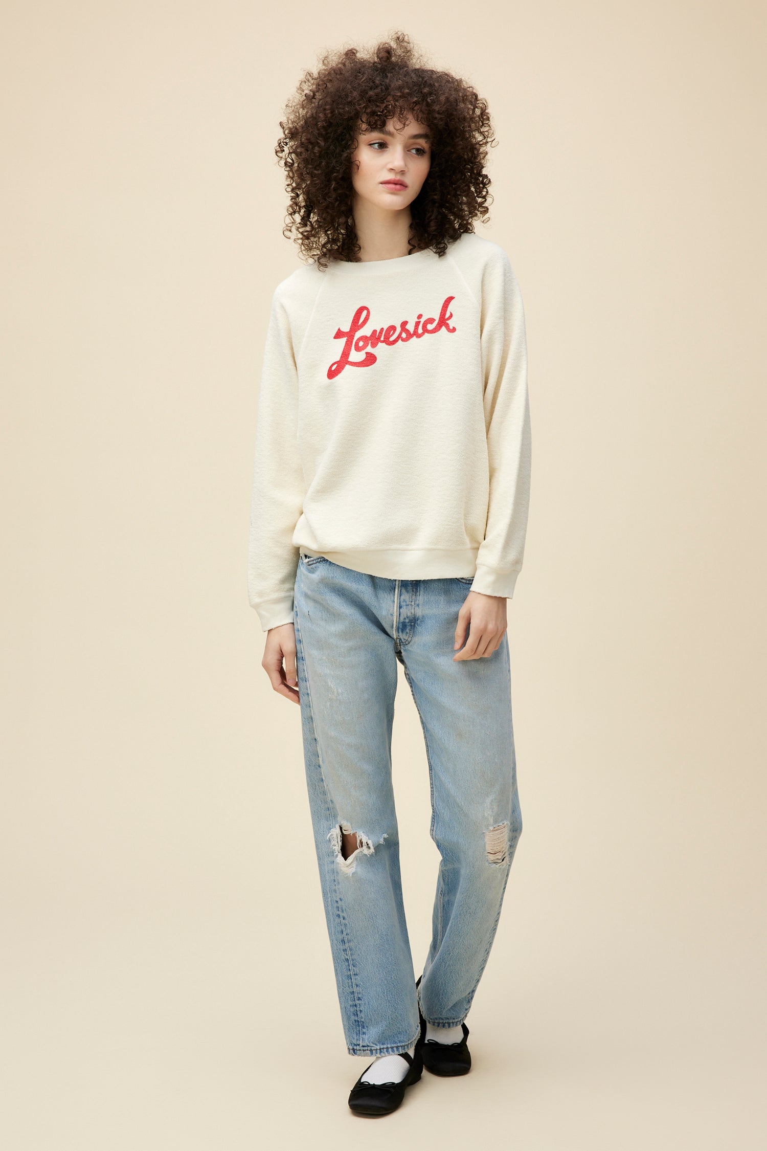 A curly-haired model wearing a reverse brushed fleece sweatshirt stamped with 'lovesick' red script on the front.