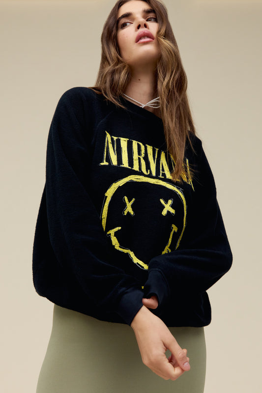 A model featuring a black crew stamped with "Nirvana" and the endlessly popular smiley face logo lands center chest on this reverse raglan crew in a sketch-like technique printed with a thicker ink to give it that hand painted look and feel. 
