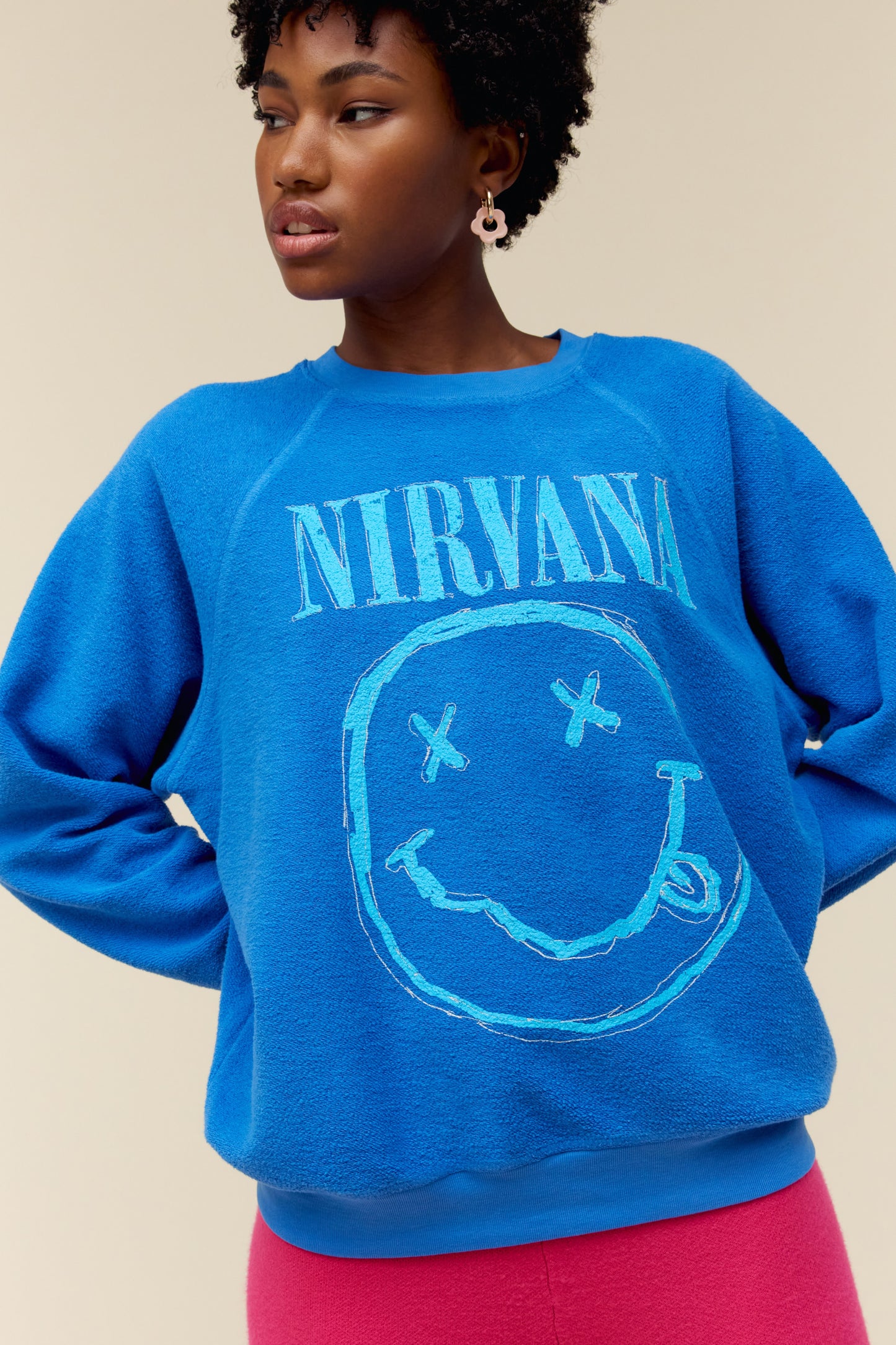 A model featuring a washed cobalt colored crew stamped with "Nirvana" and the endlessly popular smiley face logo lands center chest on this reverse raglan crew in a sketch-like technique printed with a thicker ink to give it that hand painted look and feel. 