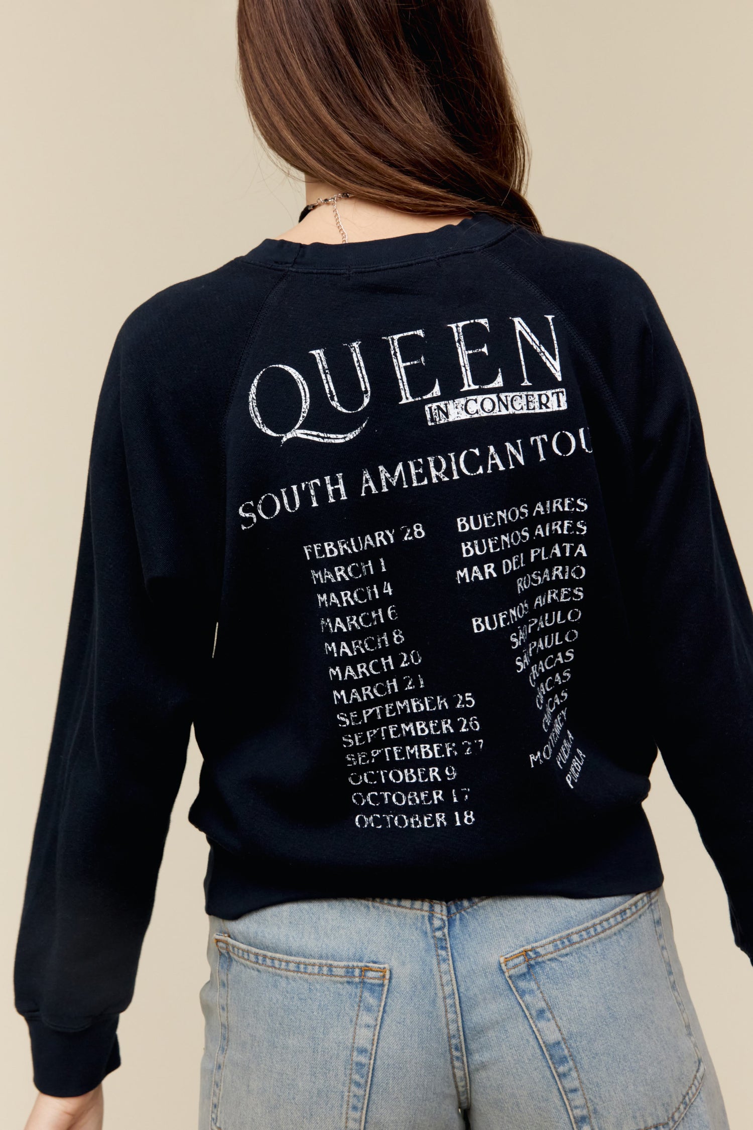 A model featuring a black raglan crew stamped with Queen in front and a list of tour dates and places at the back.