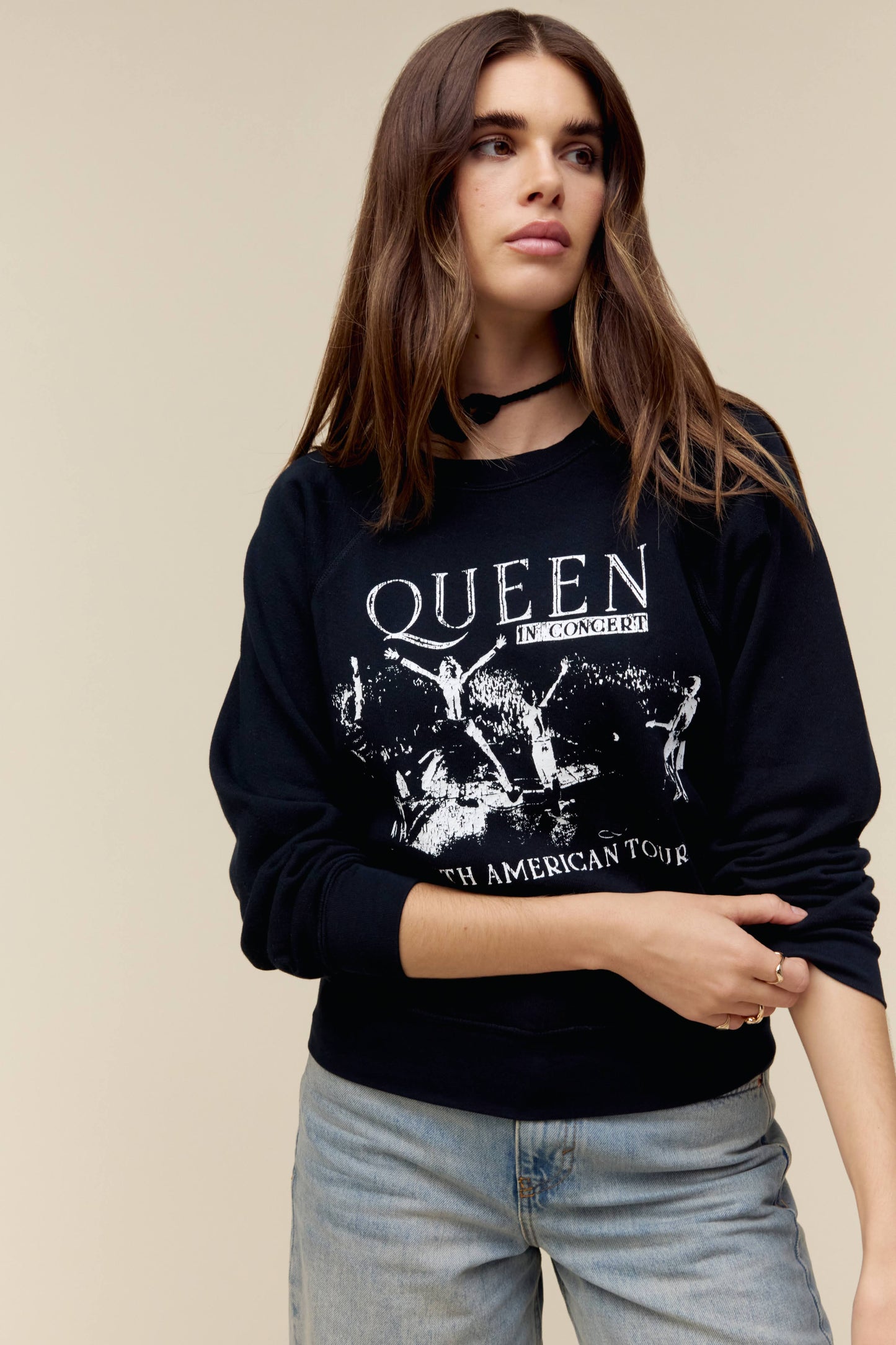 A model featuring a black raglan crew stamped with Queen in front and a list of tour dates and places at the back.