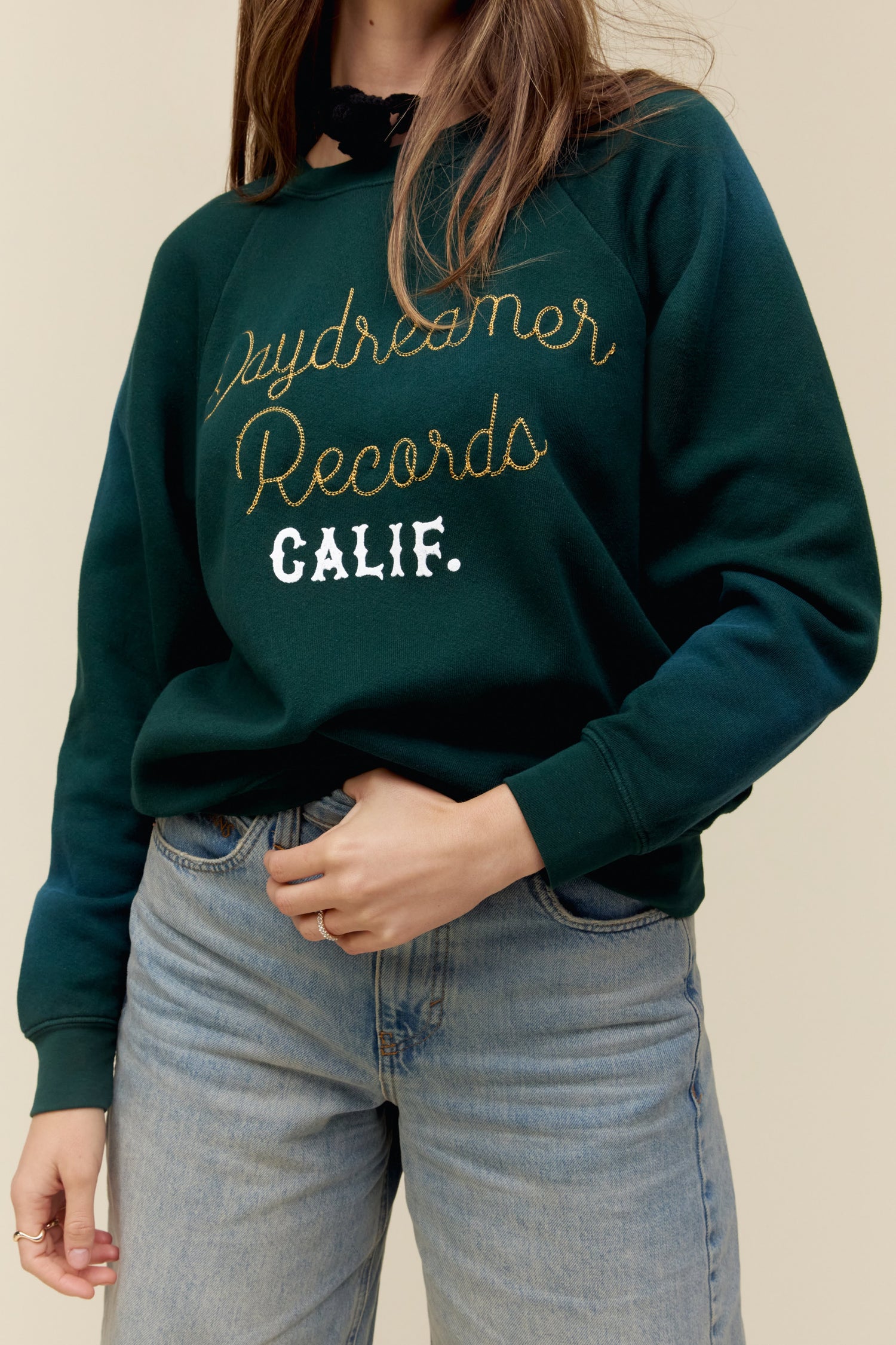 A dark-haired model featuring a green longsleeve stamped with Daydreamer Records in golden cutsive font and calif.