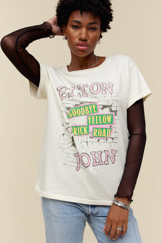A model featuring a white tee featuring motifs from Elton John's Goodbye, Yellow Brick Road album's original cover, designed with a brick road graphic and accented with rhinestones.