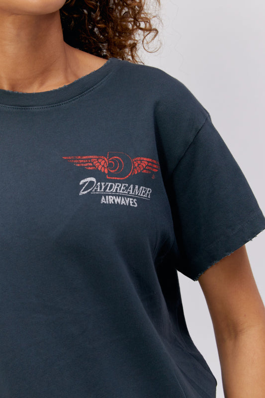 A curly-haired model featuring a black tee stamped with 'Daydreamer Airwaves' and the daydreamer logo with wings front and back.