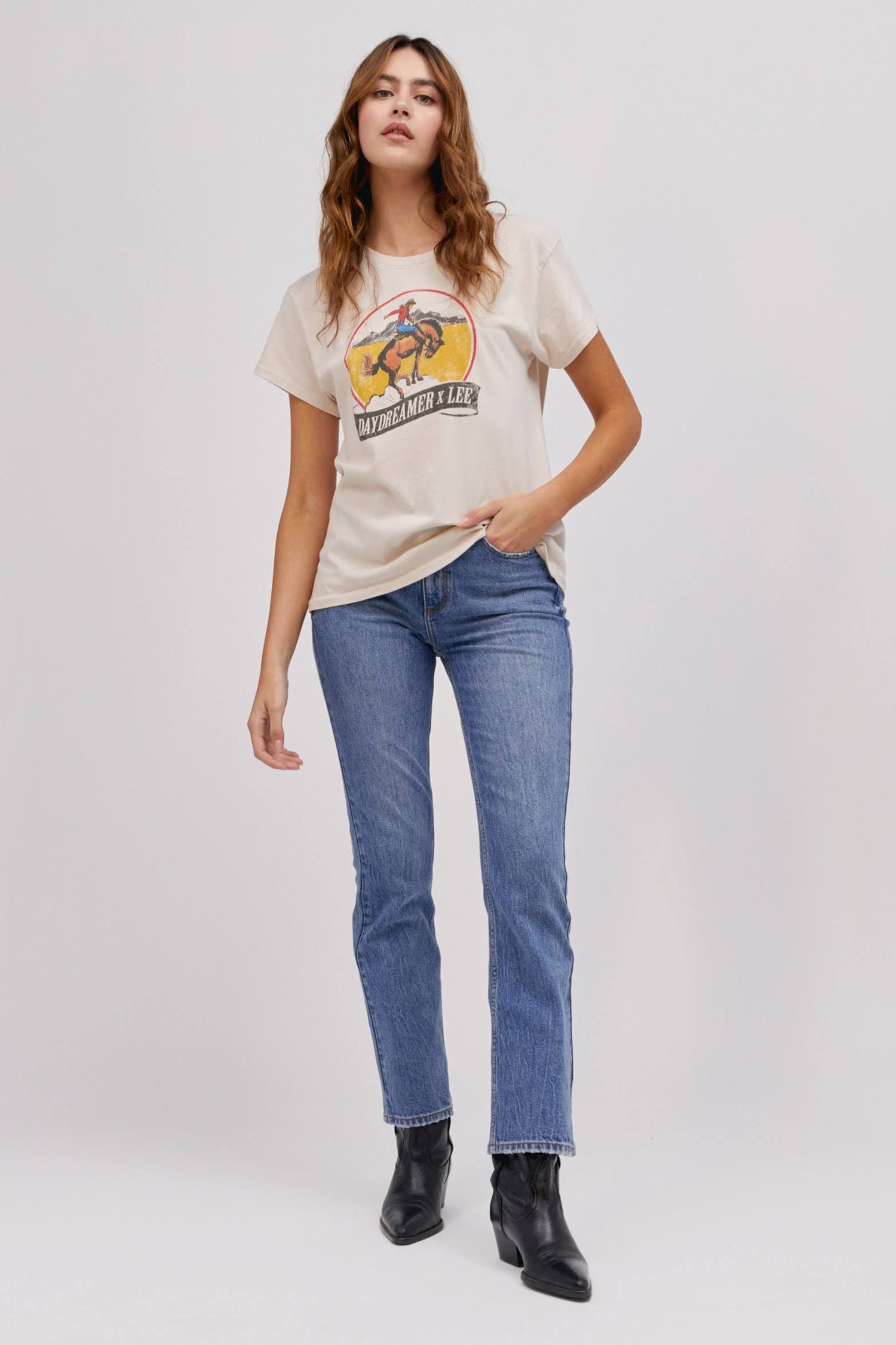 A curly-haired model featuring a white tour tee designed with a fresh rendition of a tried and true Lee vintage rodeo graphic hits a relaxed fit, Tour Tee.