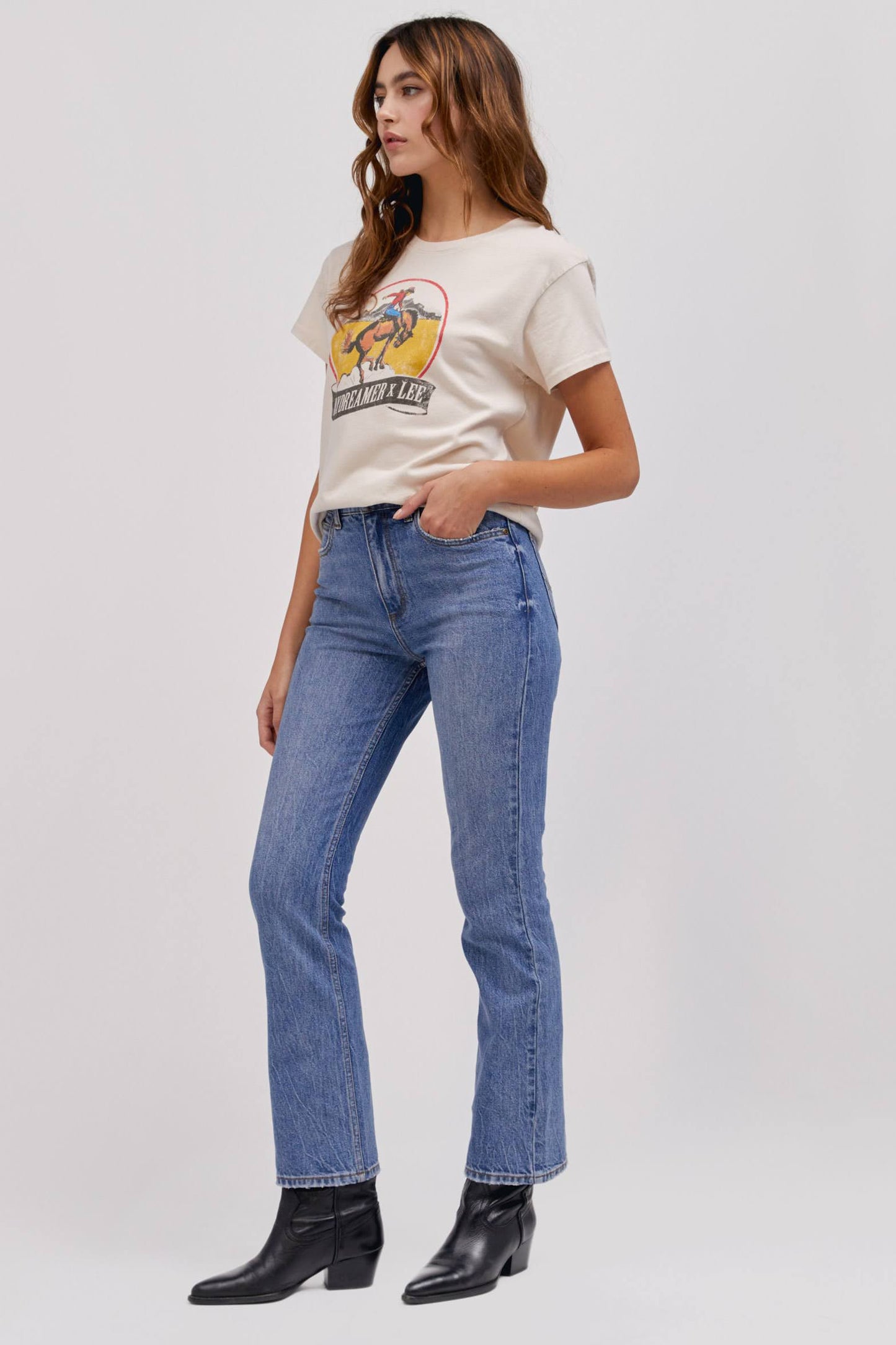 A curly-haired model featuring a white tour tee designed with a fresh rendition of a tried and true Lee vintage rodeo graphic hits a relaxed fit, Tour Tee.