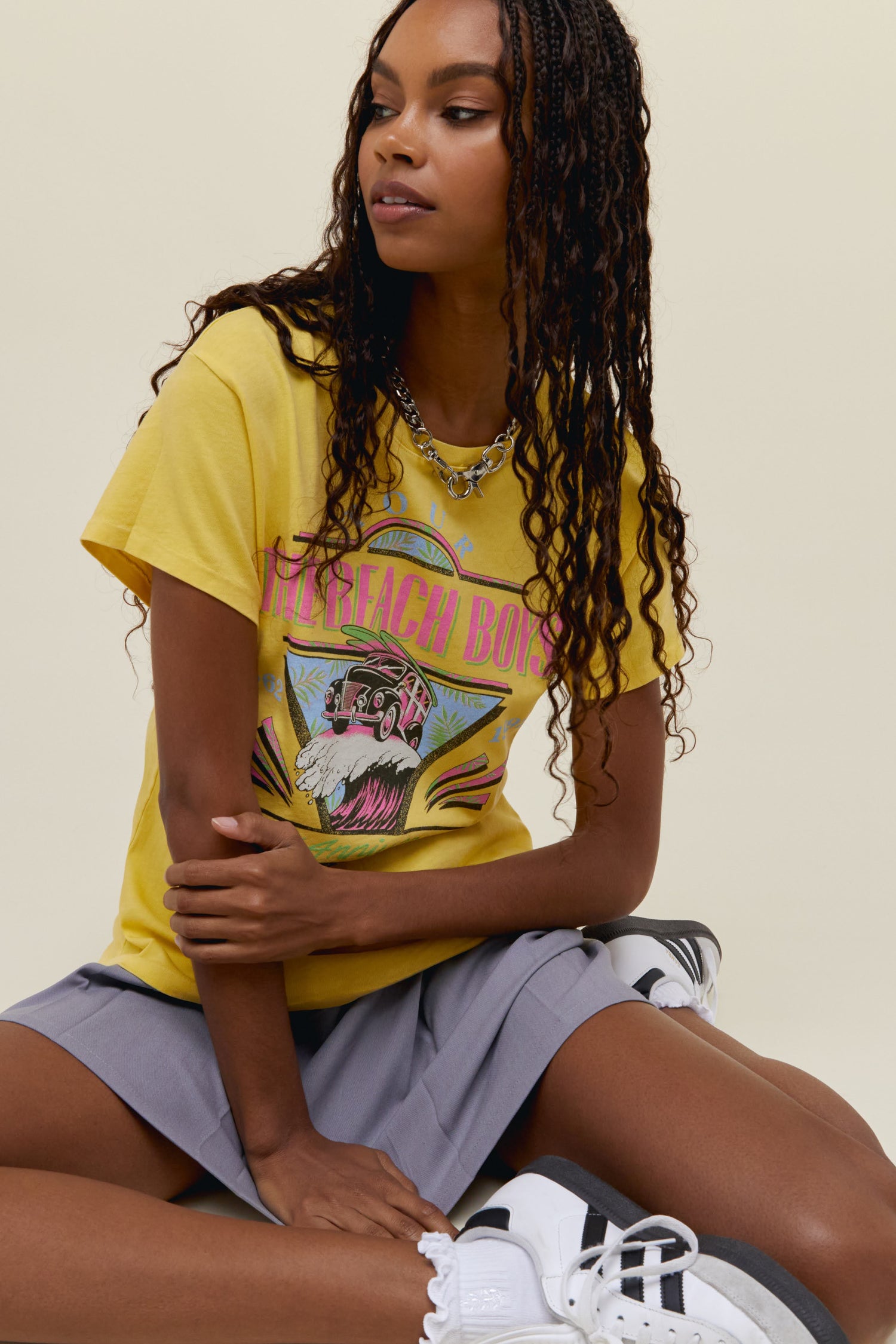 A model featuring a  yellow tour tee stamped with 'The  Beach Boys' in pink font and designed with a graphic car on a wave