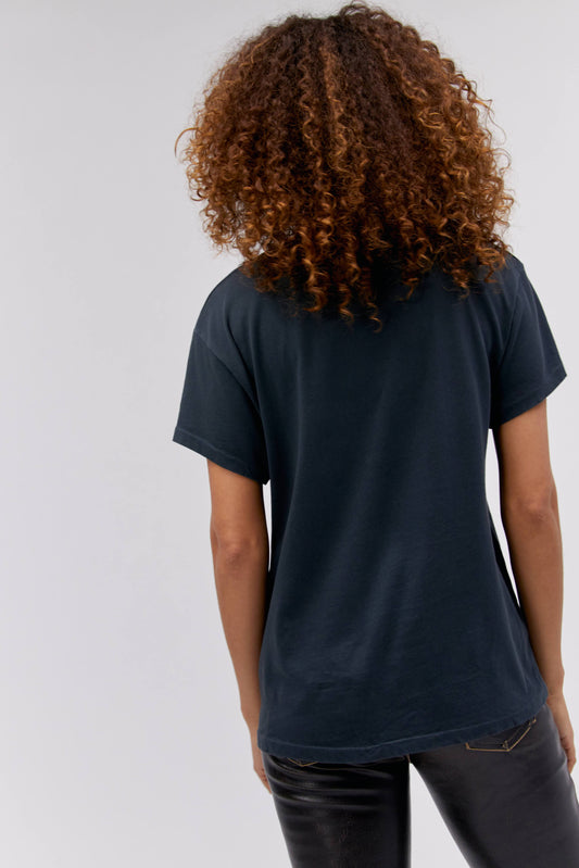 A curly-haired model featuring a black tee stamped with 'Willie Nelson' and designed with a bird with 'Abott Texas' on its mouth.