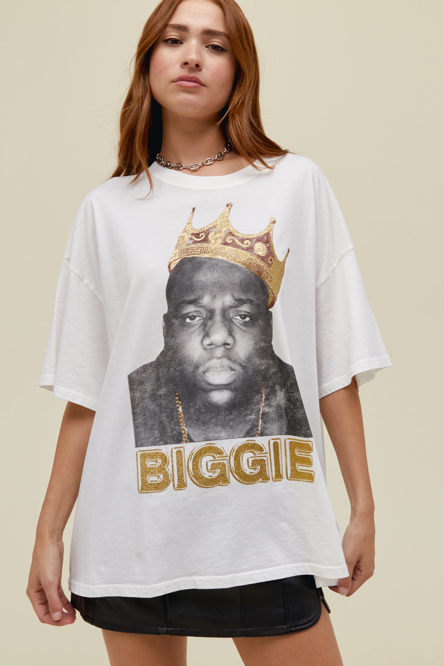 A straight-haired model featuring a white tee stamped with 'Biggie' and a crown graphic accented in gold with an authentic portrait of the rapper.