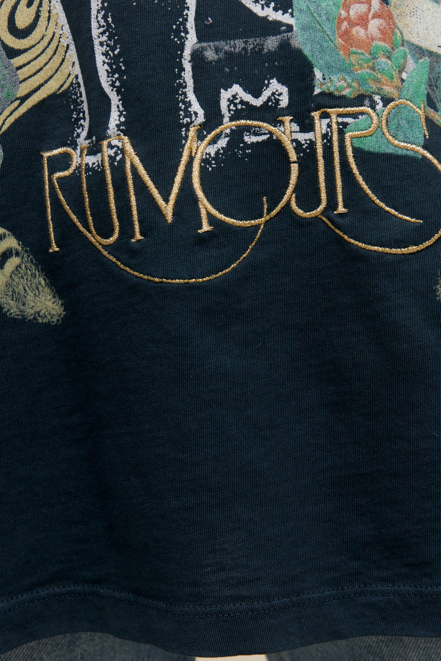 Short-haired model wearing an oversized Fleetwood Mac graphic tee with gold embroidery and floral artwork