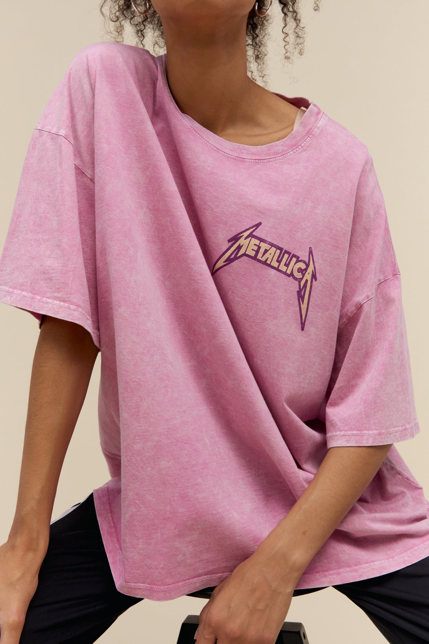 Model wearing a Metallica US Tour 1985 graphic tee with an exaggerated oversized fit and a pink acid washed colorway