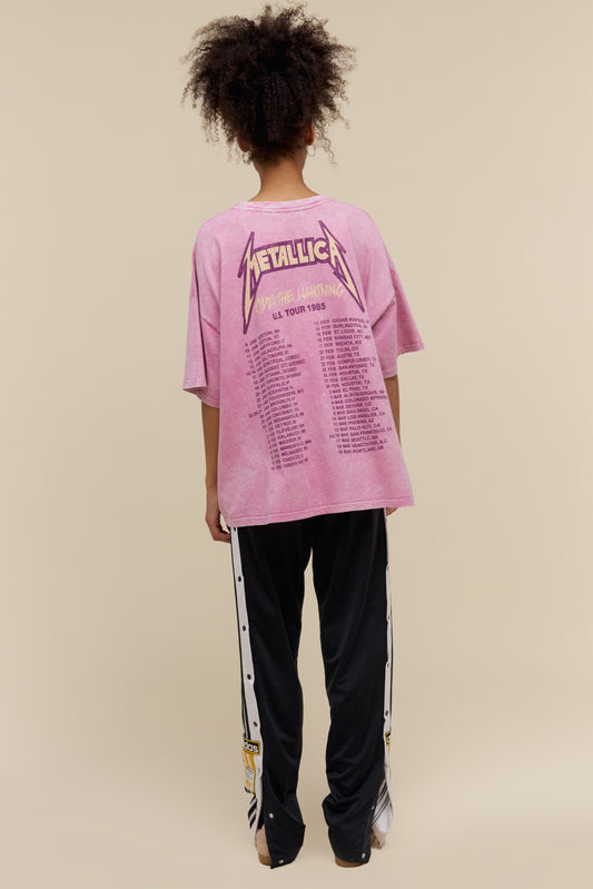 Model wearing a Metallica US Tour 1985 graphic tee with an exaggerated oversized fit and a pink acid washed colorway