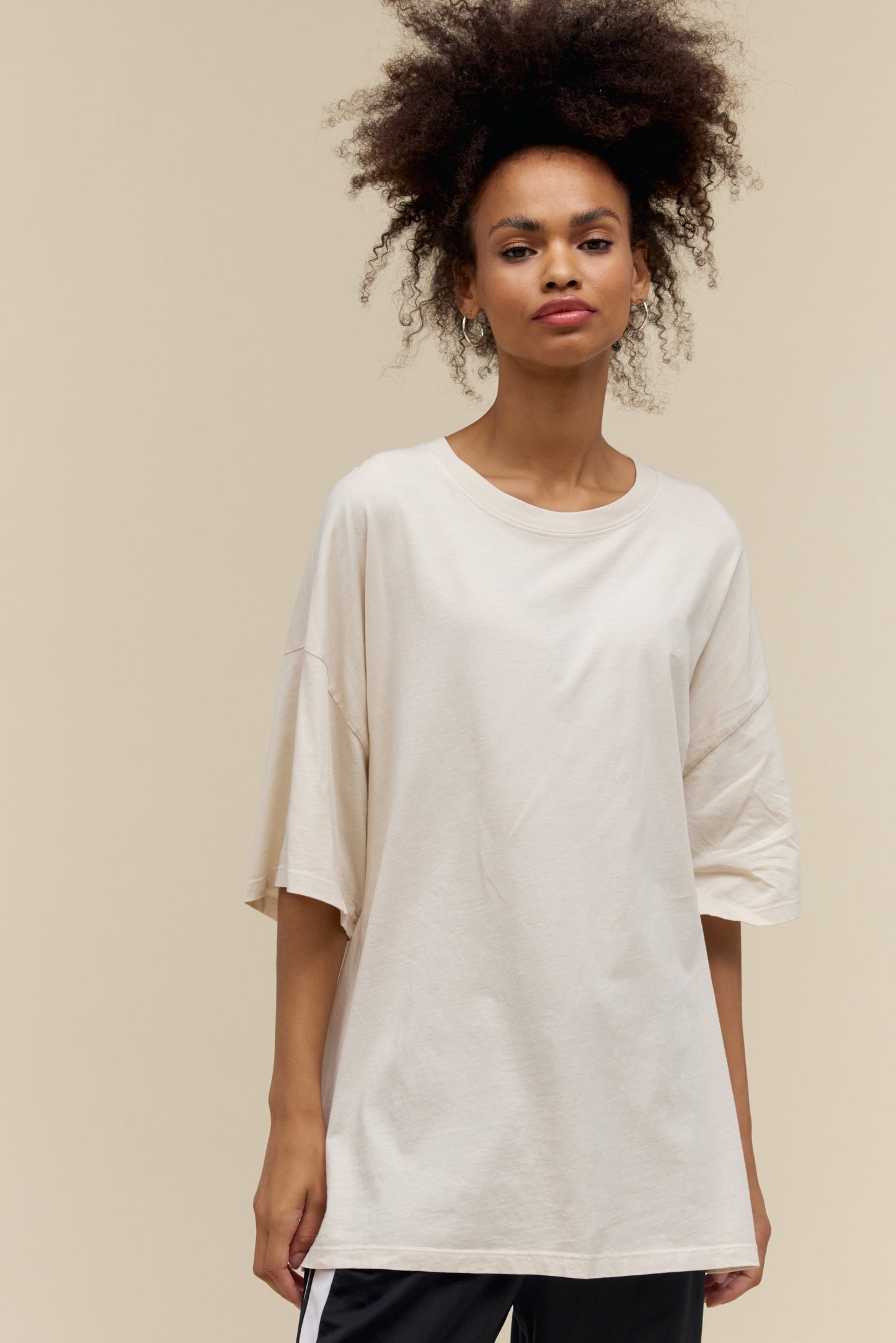 Model wearing a plain t-shirt in dirty white that has an exaggerated oversized fit
