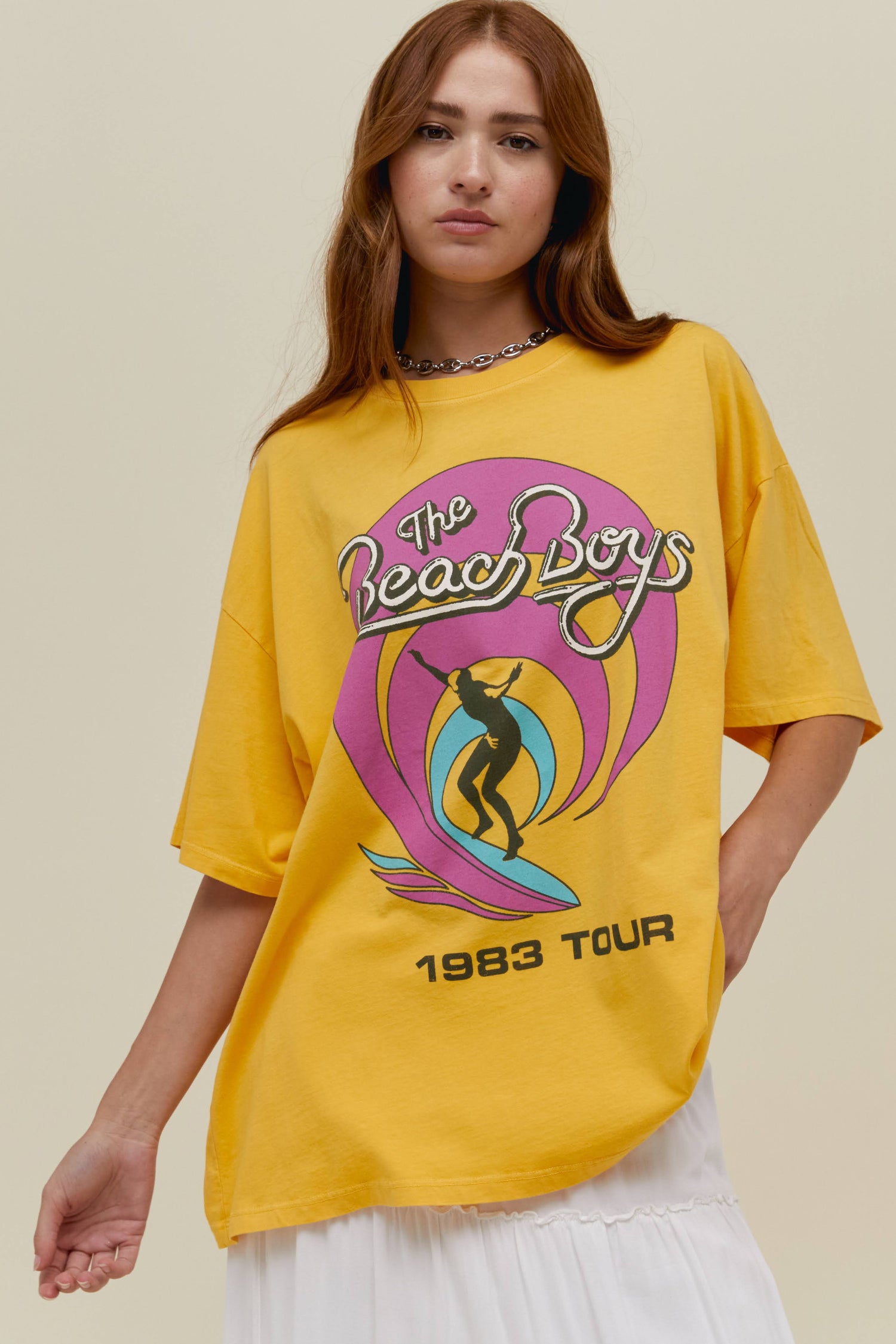 A straight-haired model featuring a dandelion tee stamped with 'The Beach Boys' and designed with the iconic surfing graphics.