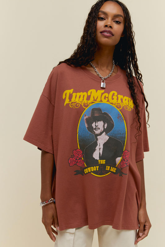 A dark-haired model featuring a reddish brown t-shirt dress adorned with Tim McGraw" on top with the graphic image of Tim Mcgraw in the center