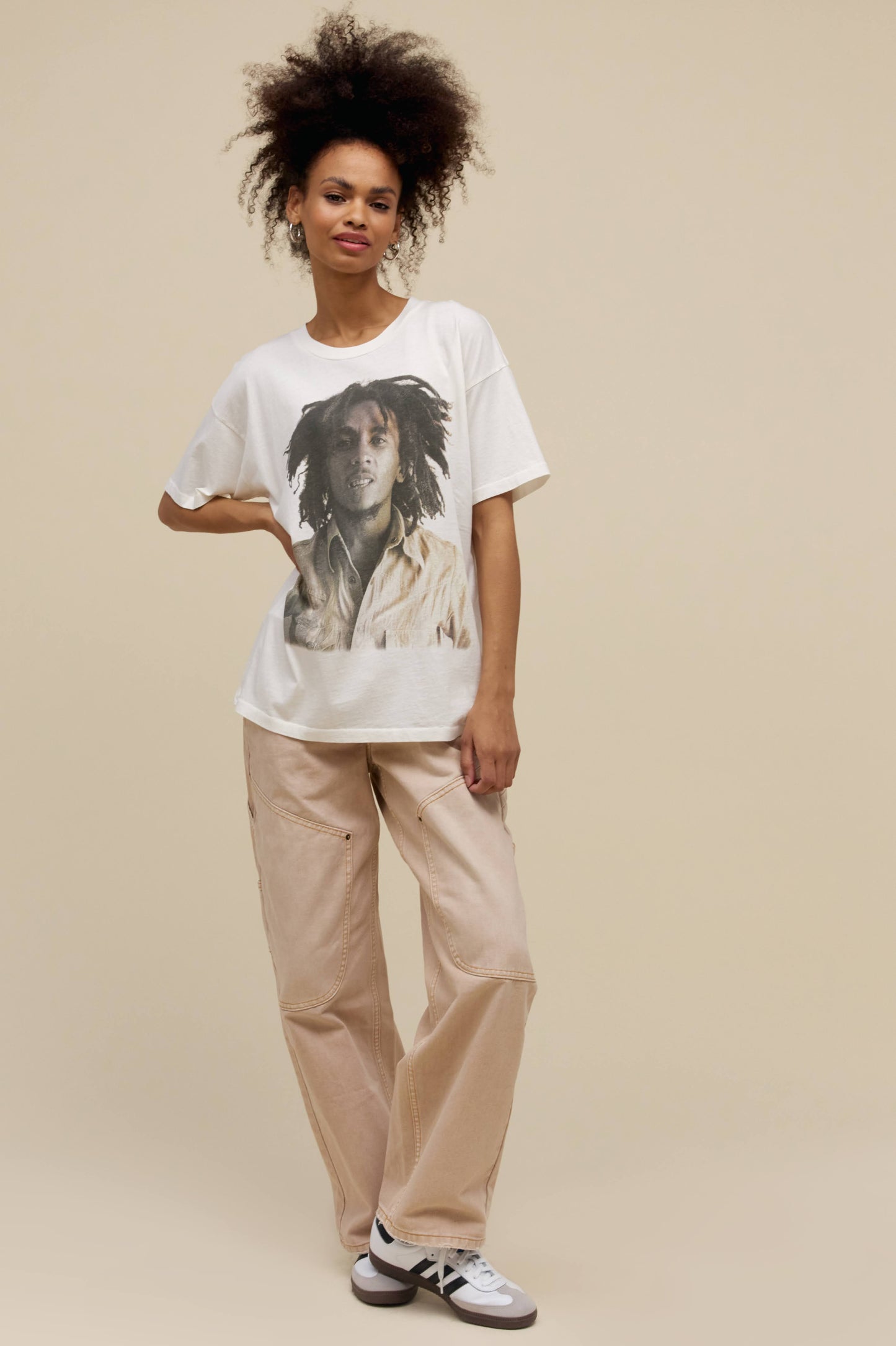 Curly-haired model wearing an oversized Bob Marley graphic tee in vintage white featuring a greyscale portrait of the artist