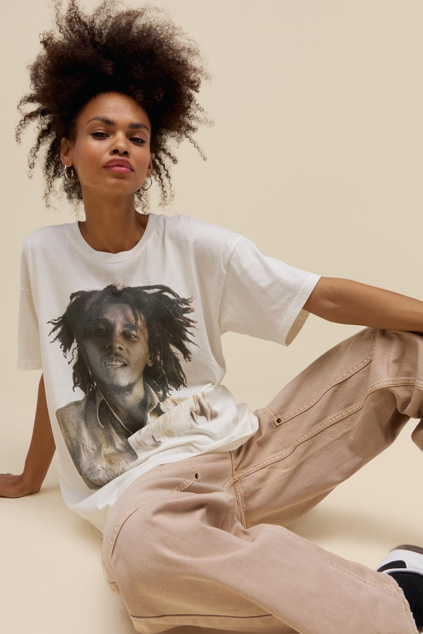 Curly-haired model wearing an oversized Bob Marley graphic tee in vintage white featuring a greyscale portrait of the artist