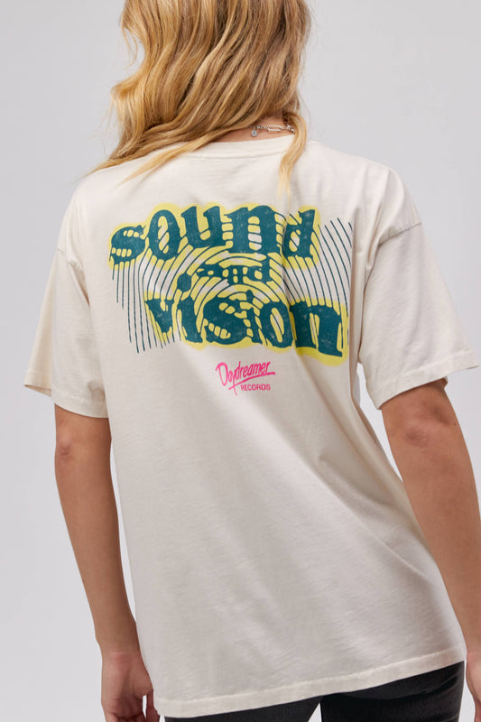 A blonde-haired model featuring a white tee stamped with 'daydreamer' and 'sound waves' at the back. It is also designed with pink and yellow graphics.