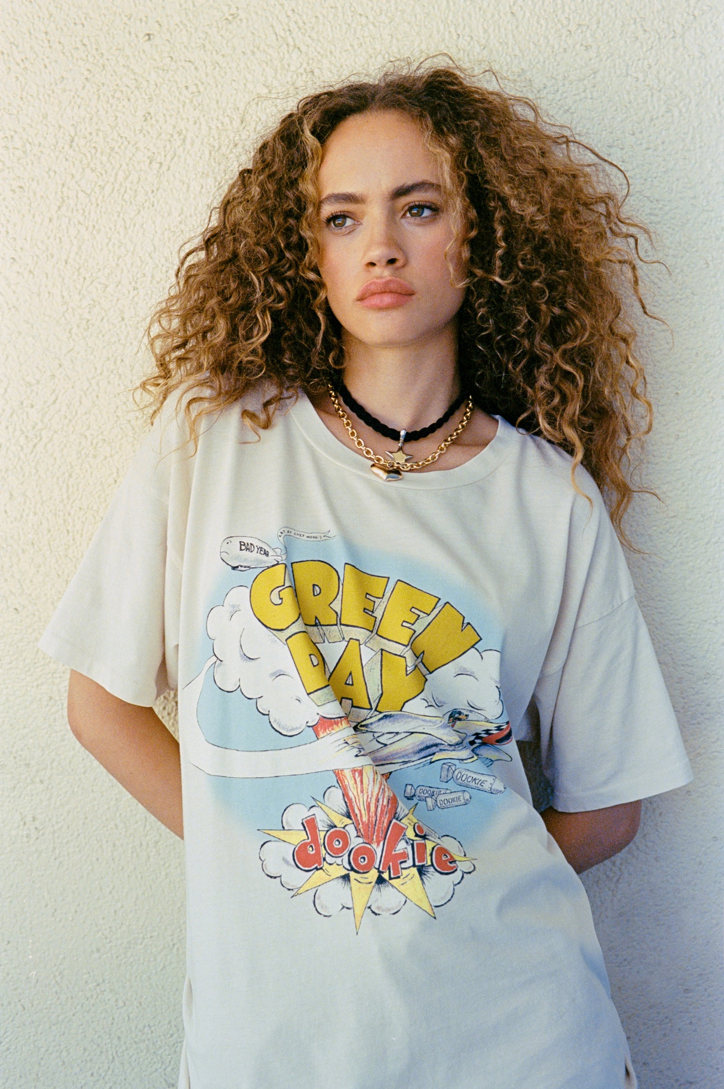 A curly-haired model featuring a white tee designed with the Green Day's album Dookie cover.