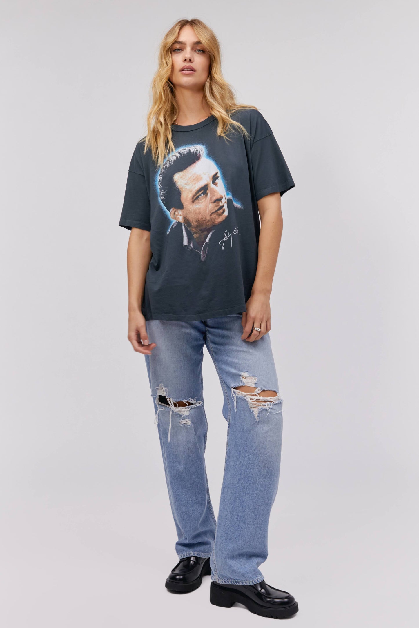 A blonde-haired model featuring a black tee designed with a portrait of Johnny Cash and stamped with 'Cash' at the back.
