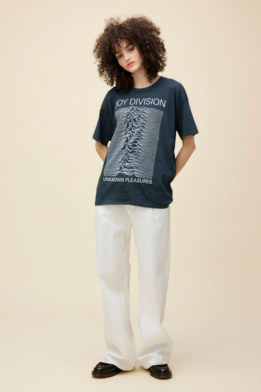 Curly-haired model wearing a Joy Division 'Unknown Pleasures' graphic tee in vintage black with a roomy fit.
