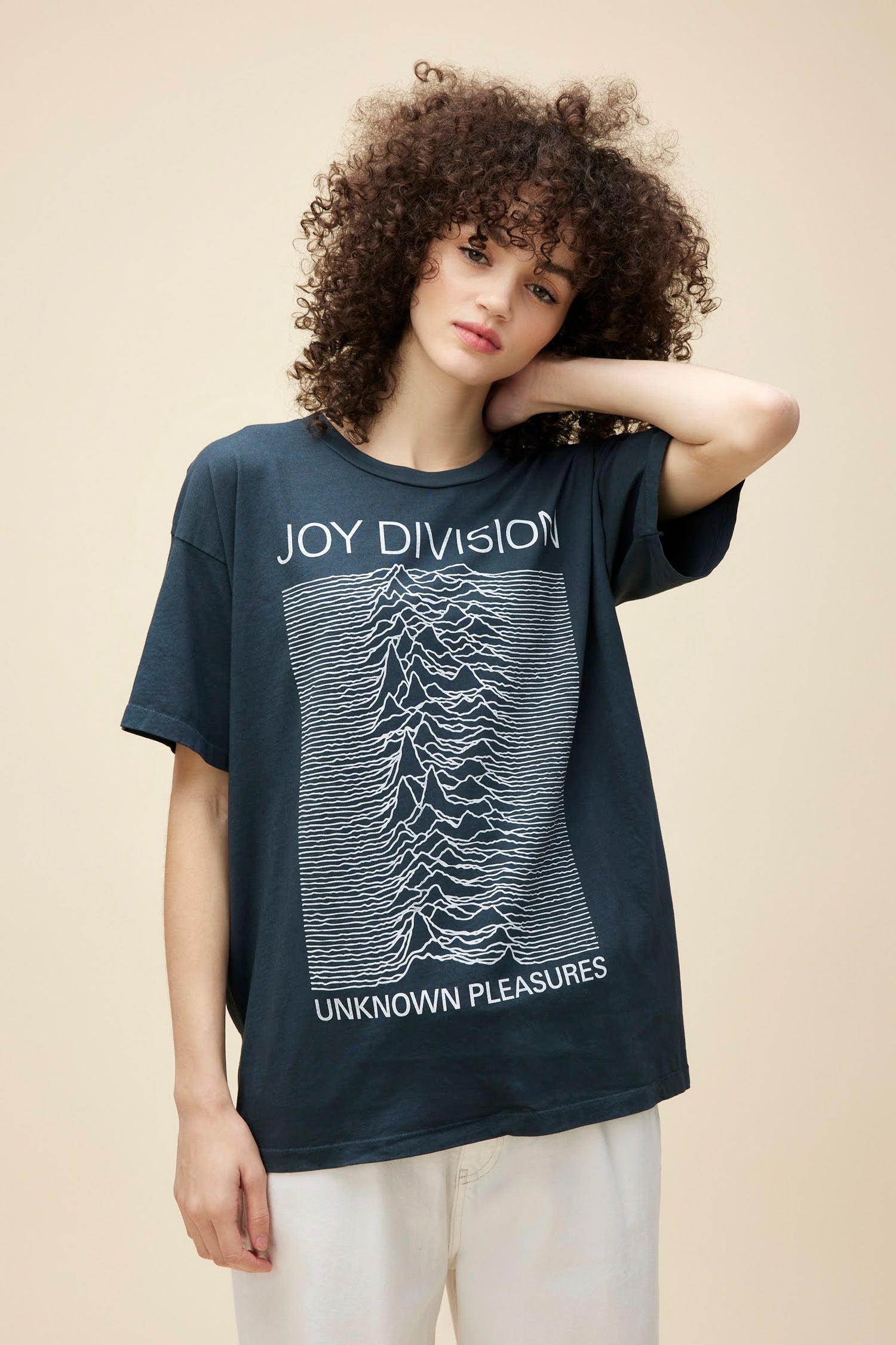 Curly-haired model wearing a Joy Division 'Unknown Pleasures' graphic tee in vintage black with a roomy fit.