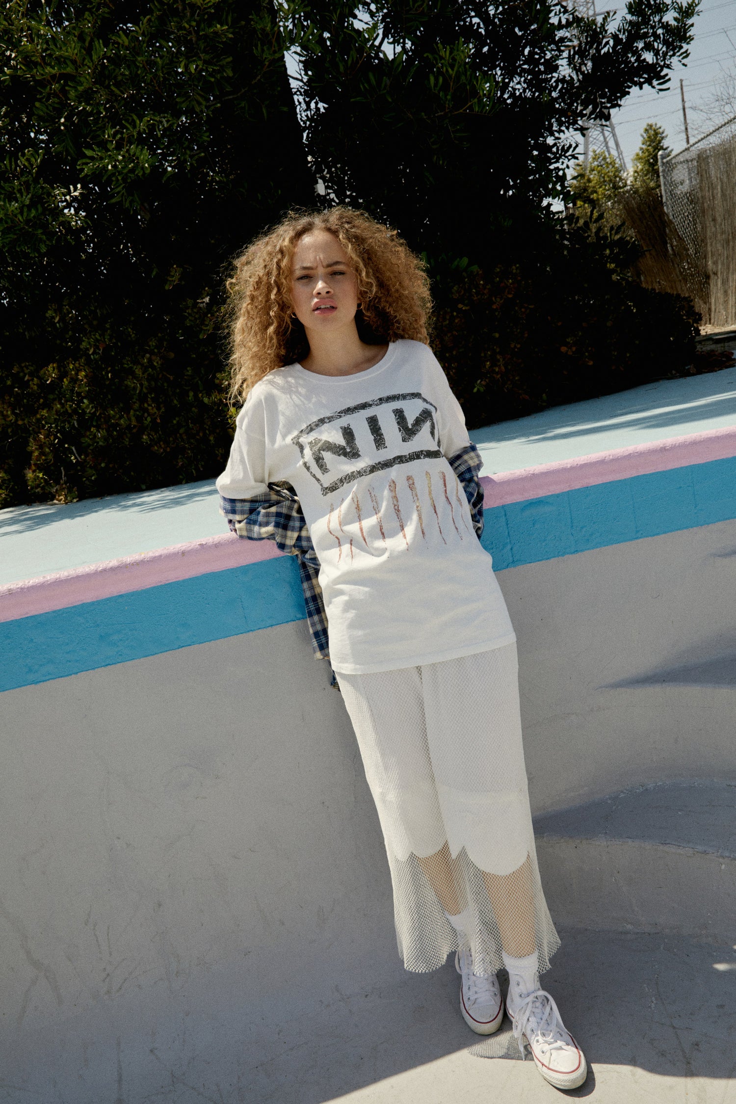 A brown curly-haired model featuring a white tee designed with their logo lands on this roomy merch tee with a tribute to one of the most important albums of the 90s,