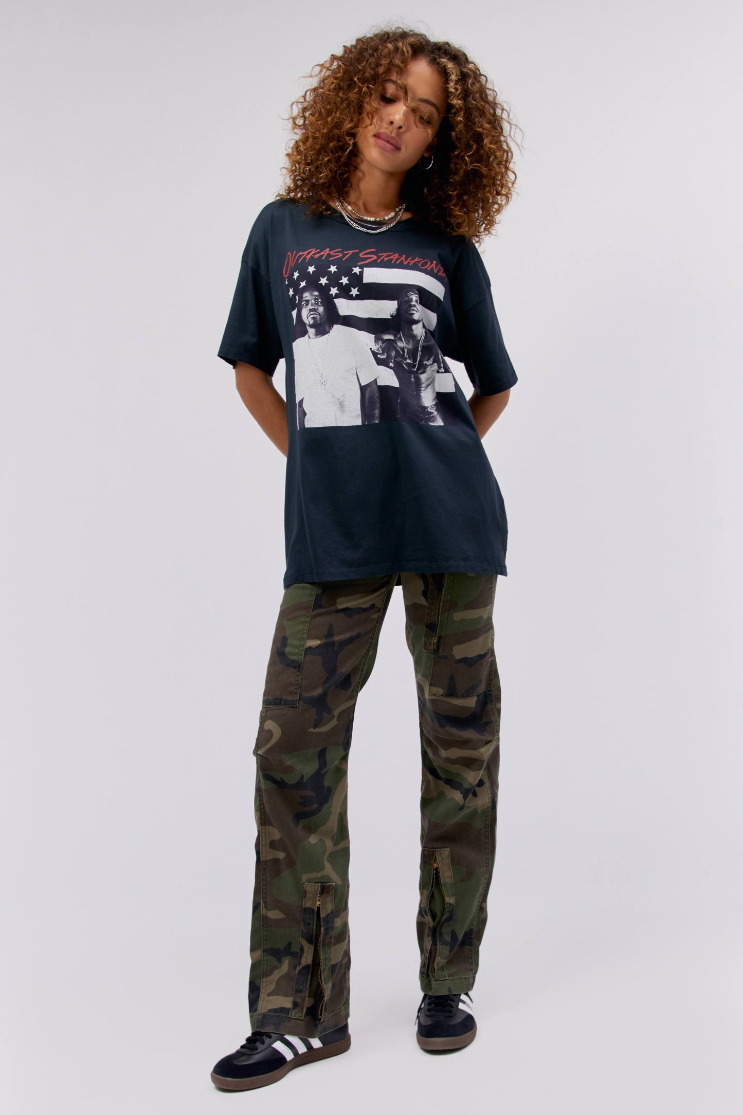 A curly-haired model featuring a black tee stamped with the duo's name and album 'Outkast Stankonia', along with a portrait of the artists in front of an American flag in black and white.