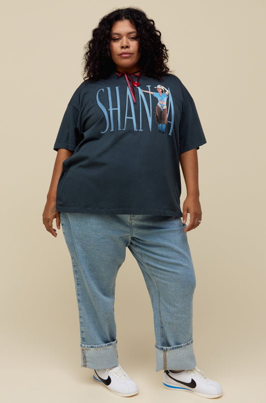 A model featuring a black tee stamped with Shania in large slim font and a portrait of the Queen of Country Pop