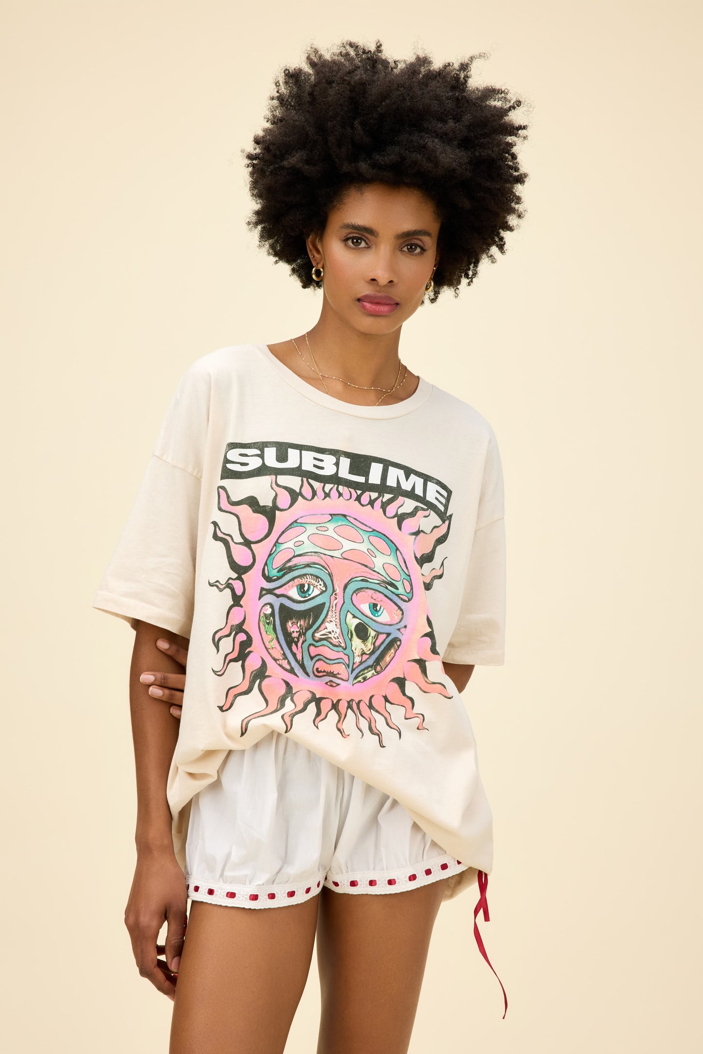 Curly-haired model wearing a roomy fit graphic tee of Sublime's 40 Oz. To Freedom sun album artwork in a dirty white colorway.