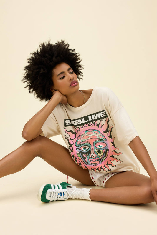 Curly-haired model wearing a roomy fit graphic tee of Sublime's 40 Oz. To Freedom sun album artwork in a dirty white colorway.