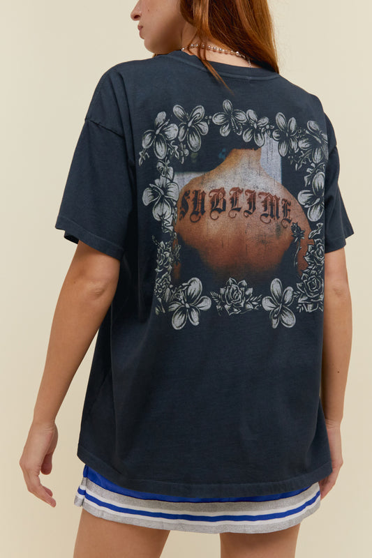 A model featuring a black merch tee stamped with 'Sublime' front and back designed with flowers.