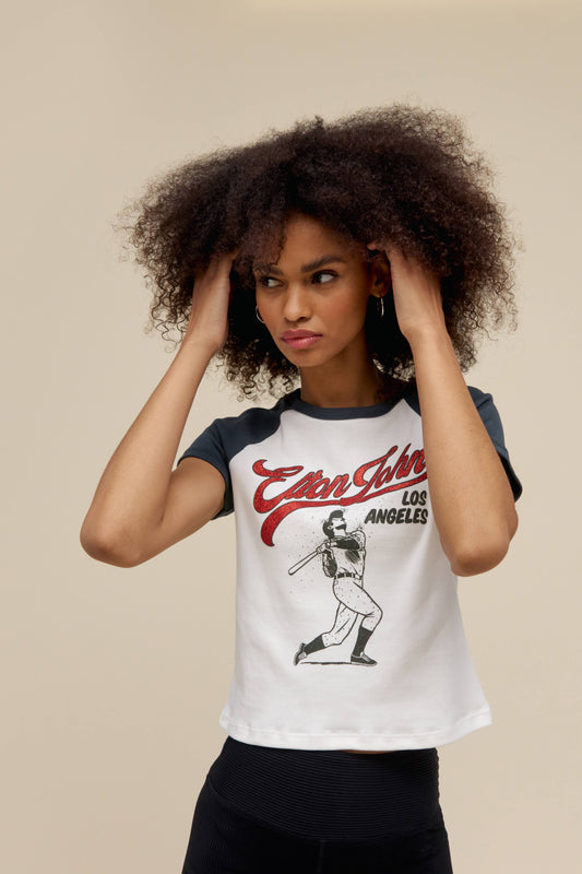 A model featuring a black and white shrunken raglan stamped with a graphic icon of Elton John on the center.