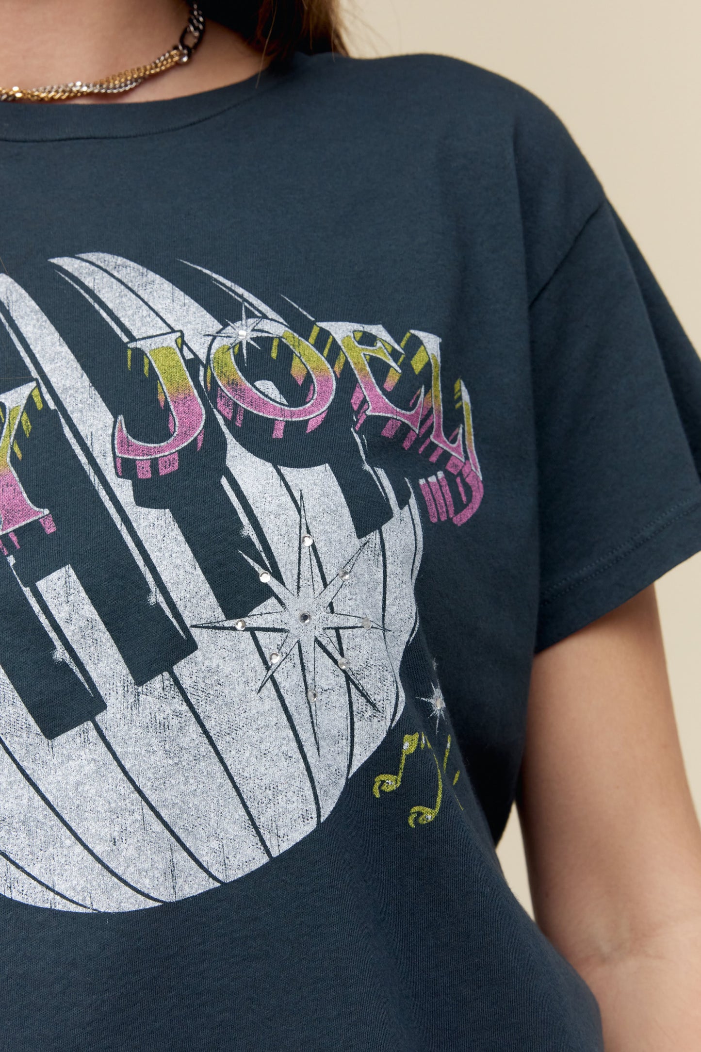 A dark-haired model featuring a black tee designed with piano keys wrapped around a disco ball and the icon’s name spelled out in bold text.