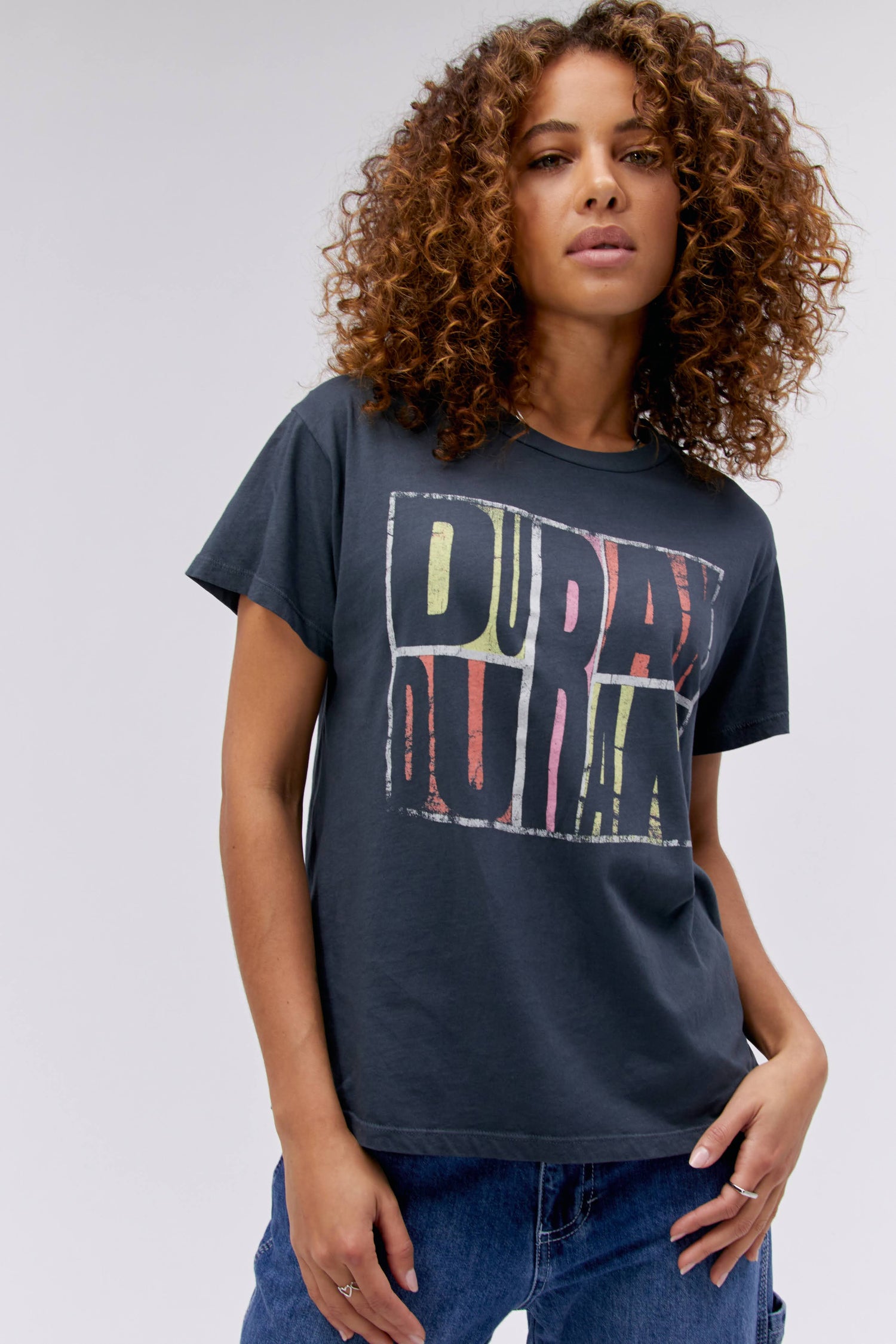 A curly-haired model featuring a black tee stamped with 'Duran Duran' in front and 'abstract', 'idealist', and 'romantic' at the back.
