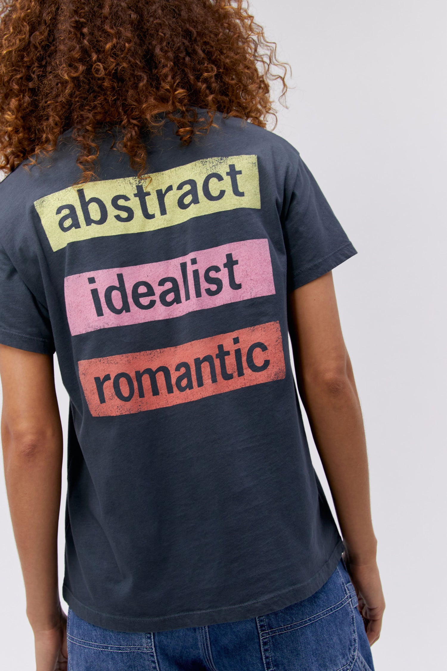 A curly-haired model featuring a black tee stamped with 'Duran Duran' in front and 'abstract', 'idealist', and 'romantic' at the back.