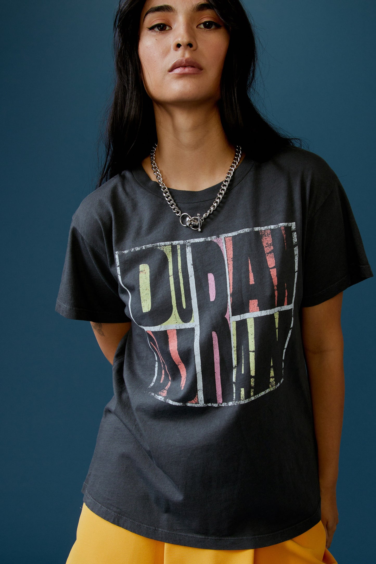 A dark-haired model featuring a black tee stamped with 'Duran Duran' in front and 'abstract', 'idealist', and 'romantic' at the back.
