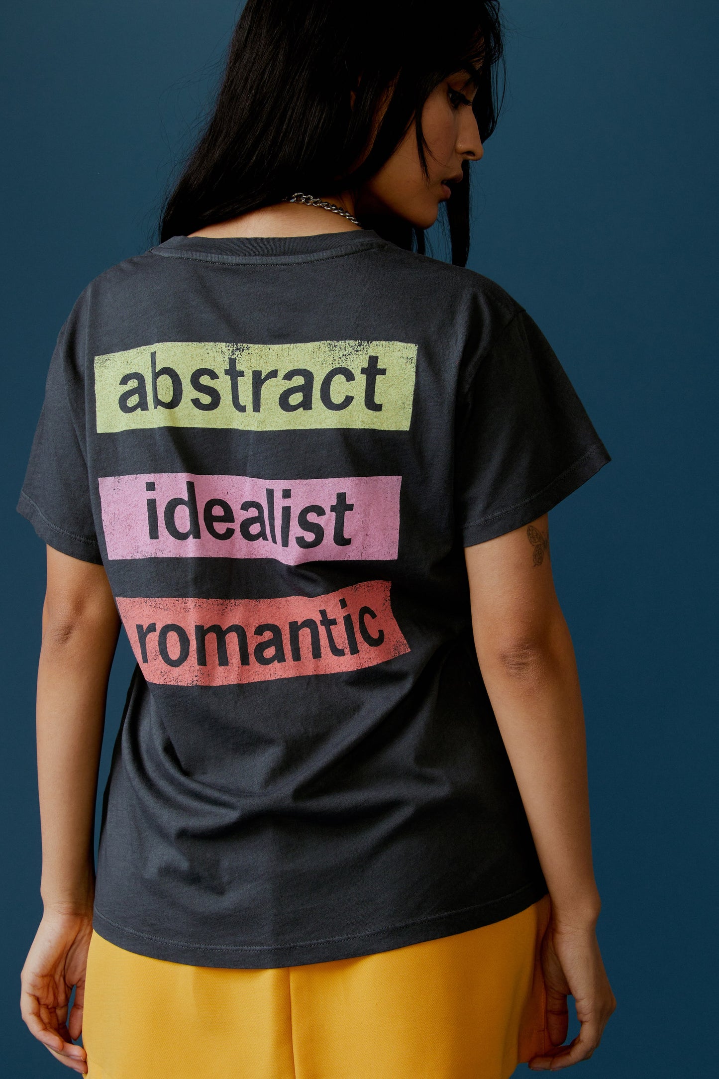 A dark-haired model featuring a black tee stamped with 'Duran Duran' in front and 'abstract', 'idealist', and 'romantic' at the back.