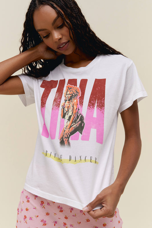 A dark-haired model wearing a white tee featuring a large font TINA in front of graphic sketch of the artist