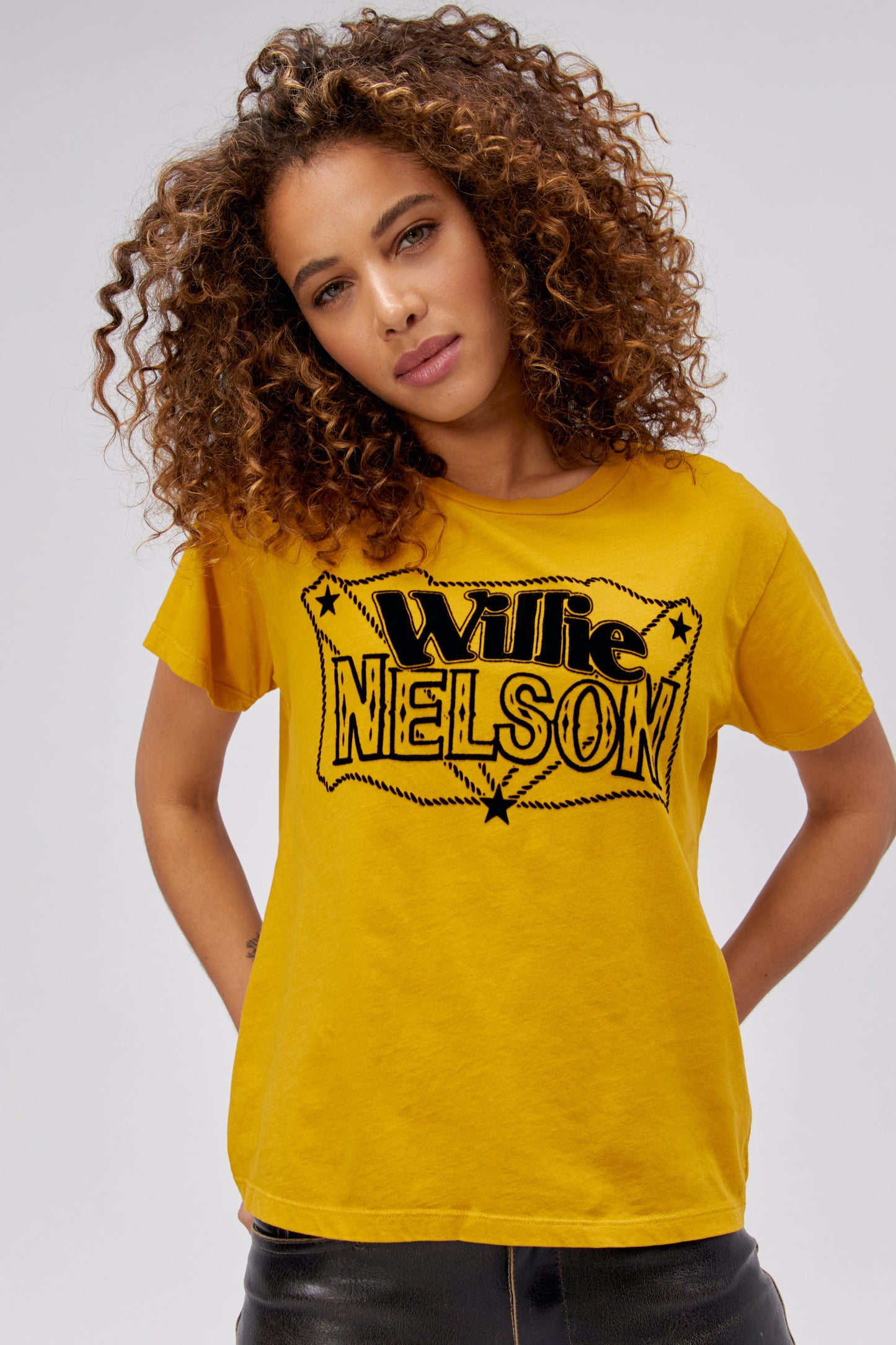 A curly-haired model featuring a golden daze tee stamped with 'Willie Nelson' in front and 'Genuine Outlaw Music' at the back.