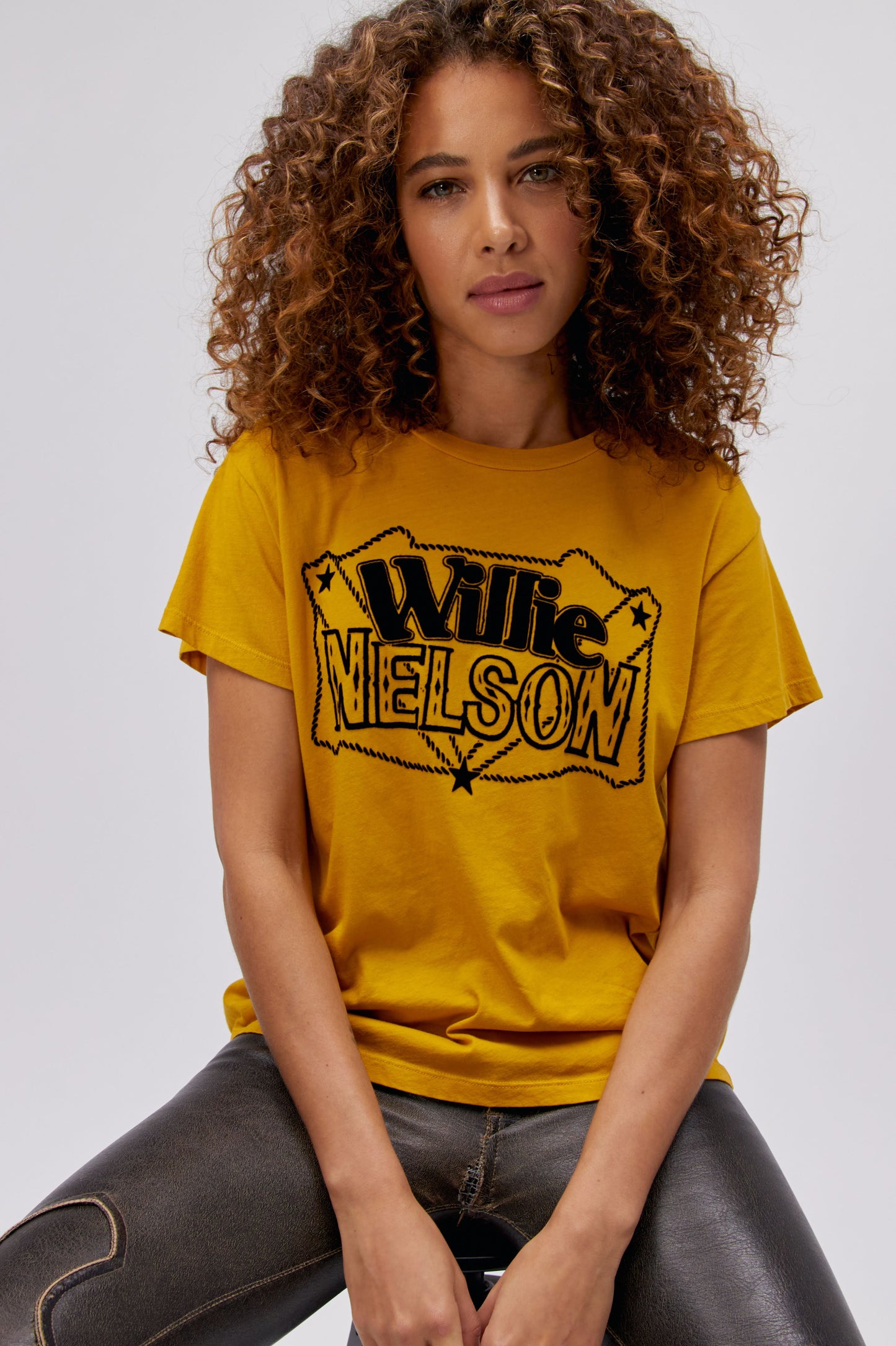 A curly-haired model featuring a golden daze tee stamped with 'Willie Nelson' in front and 'Genuine Outlaw Music' at the back.