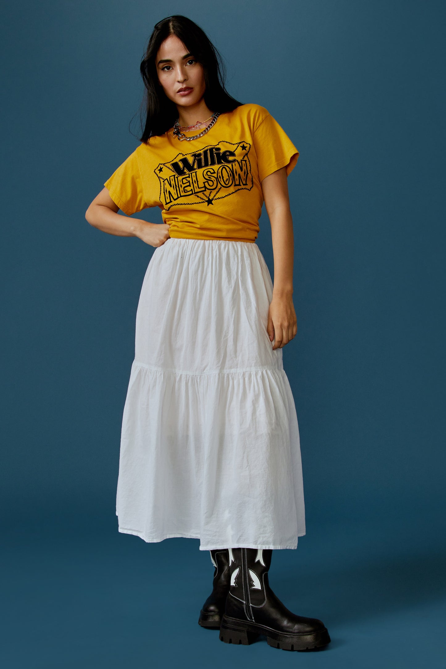 A dark-haired model featuring a golden daze tee stamped with 'Willie Nelson' in front and 'Genuine Outlaw Music' at the back.