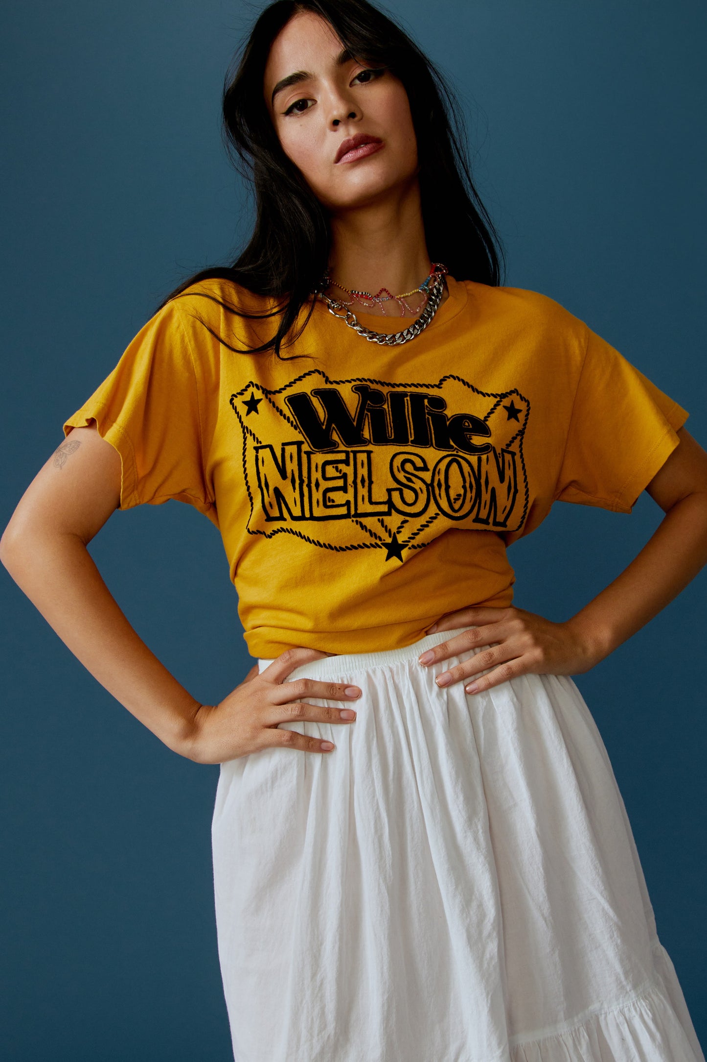 A dark-haired model featuring a golden daze tee stamped with 'Willie Nelson' in front and 'Genuine Outlaw Music' at the back.