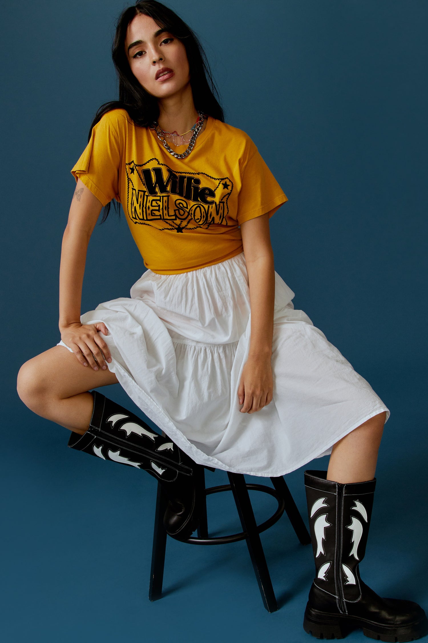 A dark-haired model featuring a golden daze tee stamped with 'Willie Nelson' in front and 'Genuine Outlaw Music' at the back.