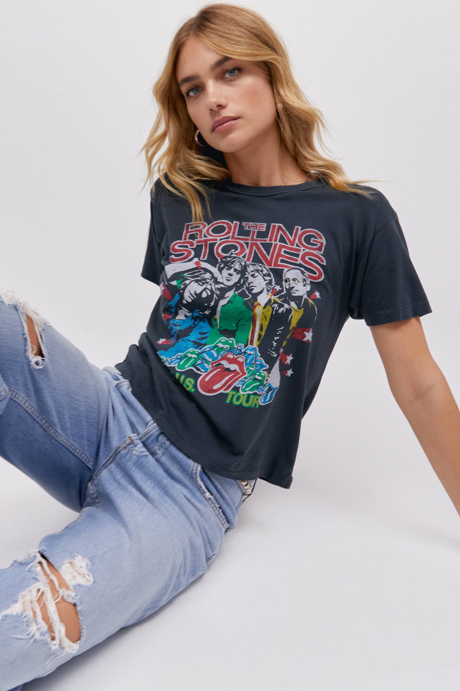 A blonde-haired model featuring a vintage black tee stamped with 'The Rolling Stones' and designed with an iconic group photo of the band.