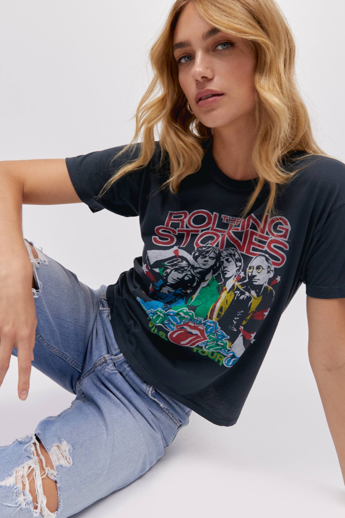 A blonde-haired model featuring a vintage black tee stamped with 'The Rolling Stones' and designed with an iconic group photo of the band.