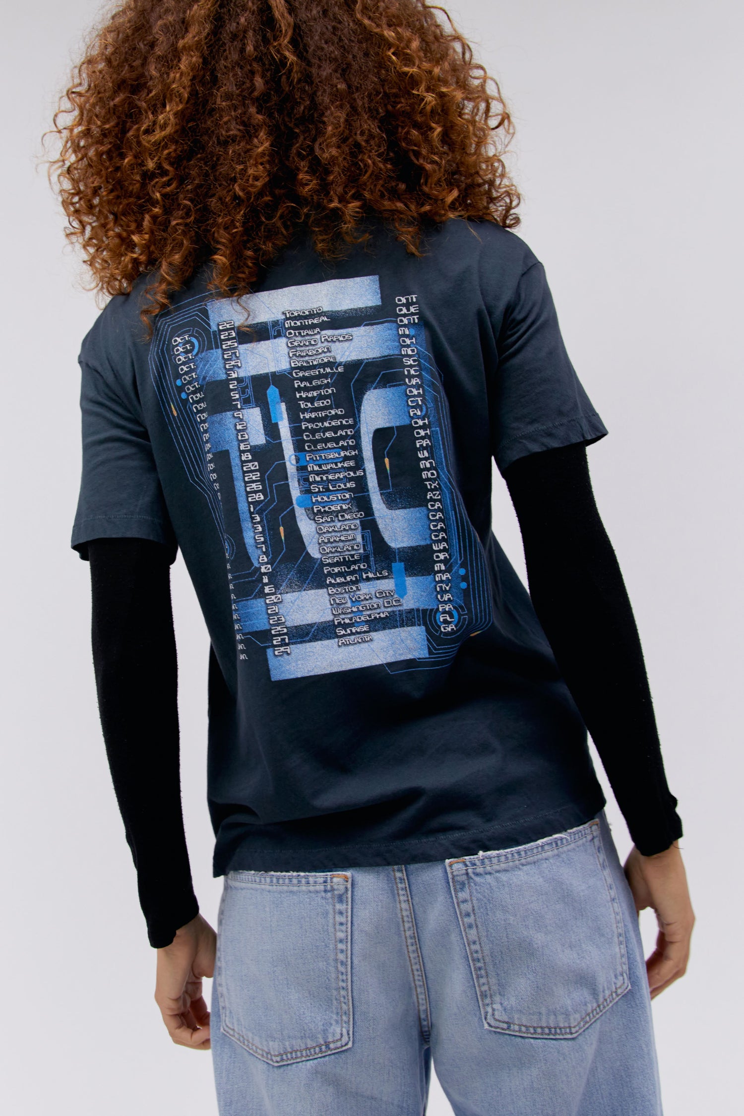 A curly-haired model featuring a black tee designed with a portrait of each member of the group and stamped with 'TLC' at the back.