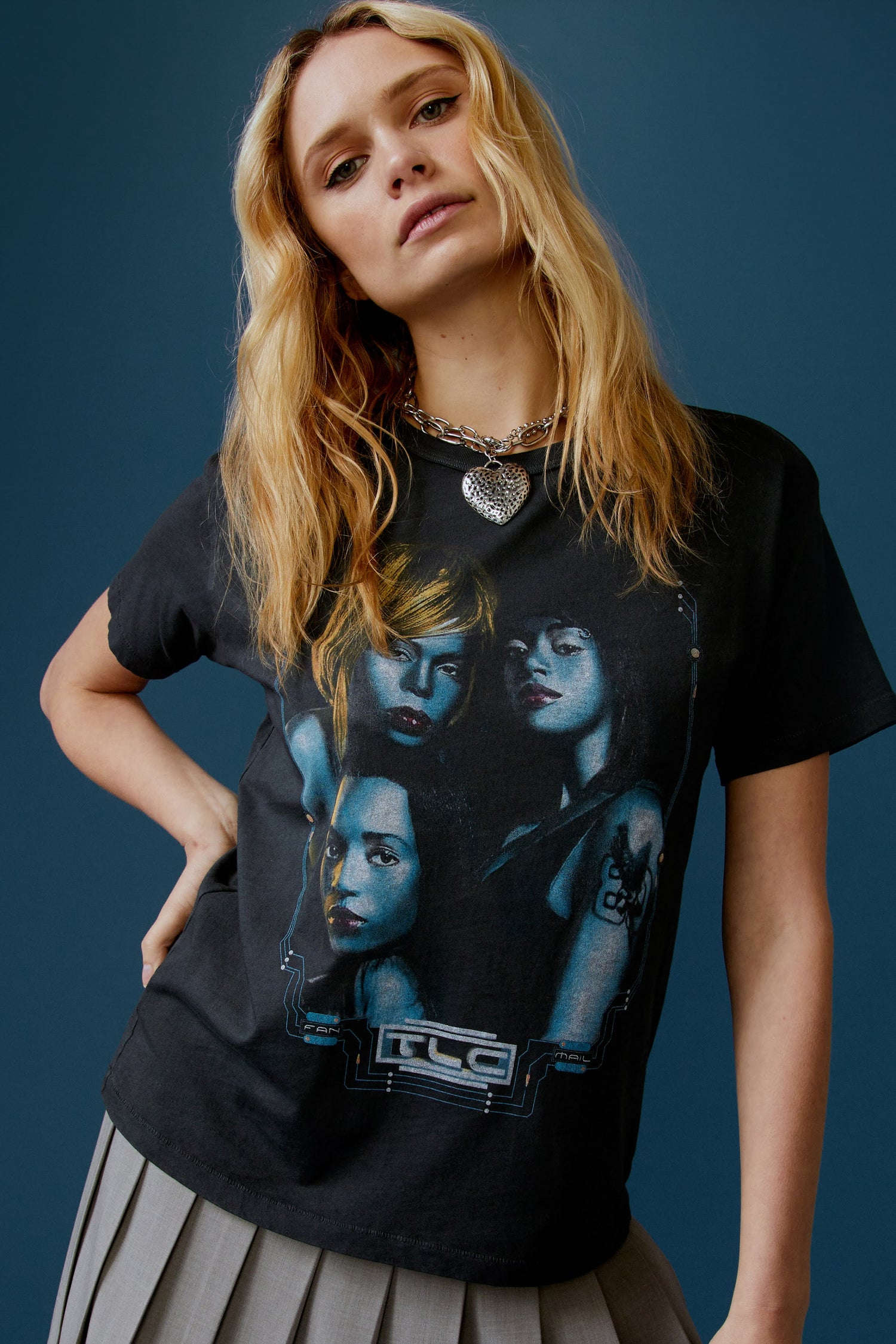 A blonde-haired model featuring a black tee designed with a portrait of each member of the group and stamped with 'TLC' at the back.