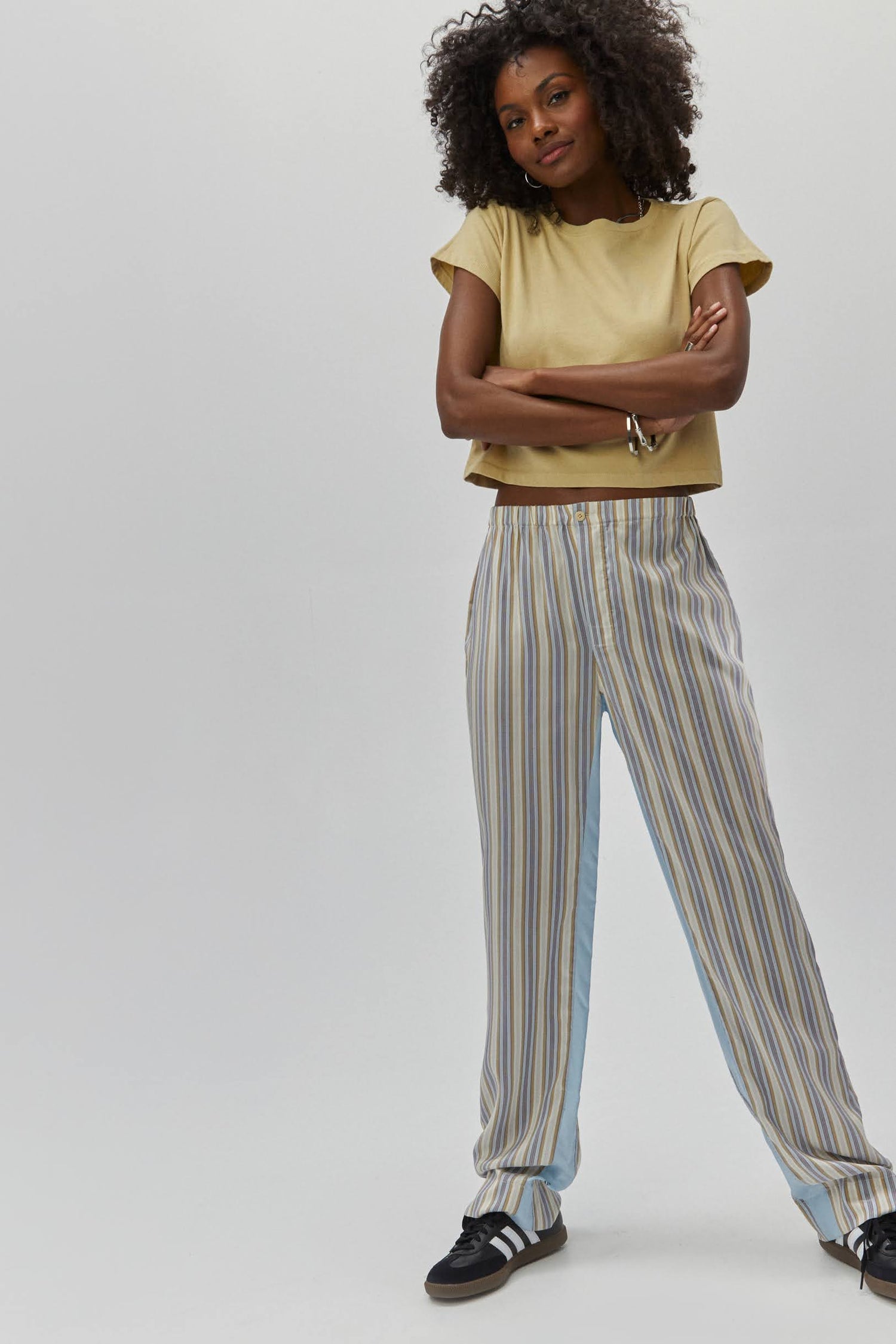 Curly haired model wearing a khaki crop tee and striped trousers.
