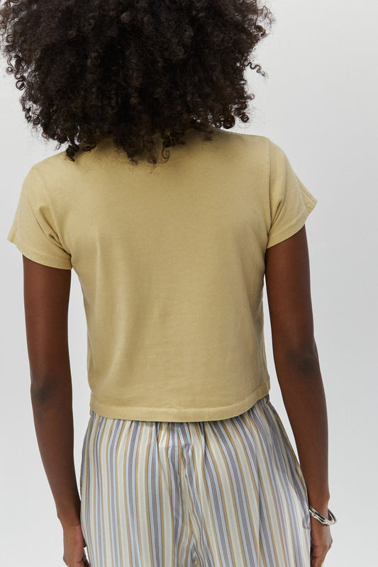 Curly haired model wearing a khaki crop tee and striped trousers.